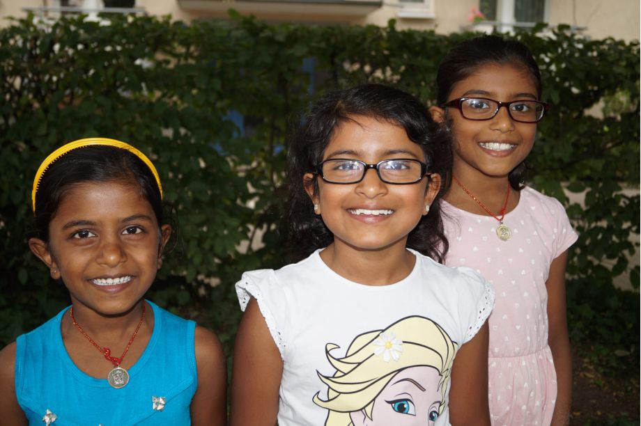 Drei fröhliche Mädchen stehen vor einer Hecke und lachen in die Kamera. Sie sind zwischen 8 und 10 Jahren alt.