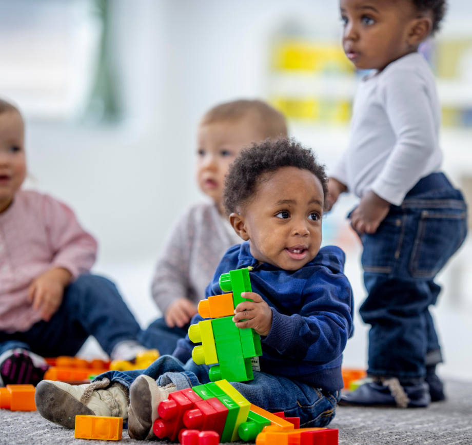 Mehrere Kleinkinder sitzen auf dem Boden und spielen mit bunten Bauklötzen.