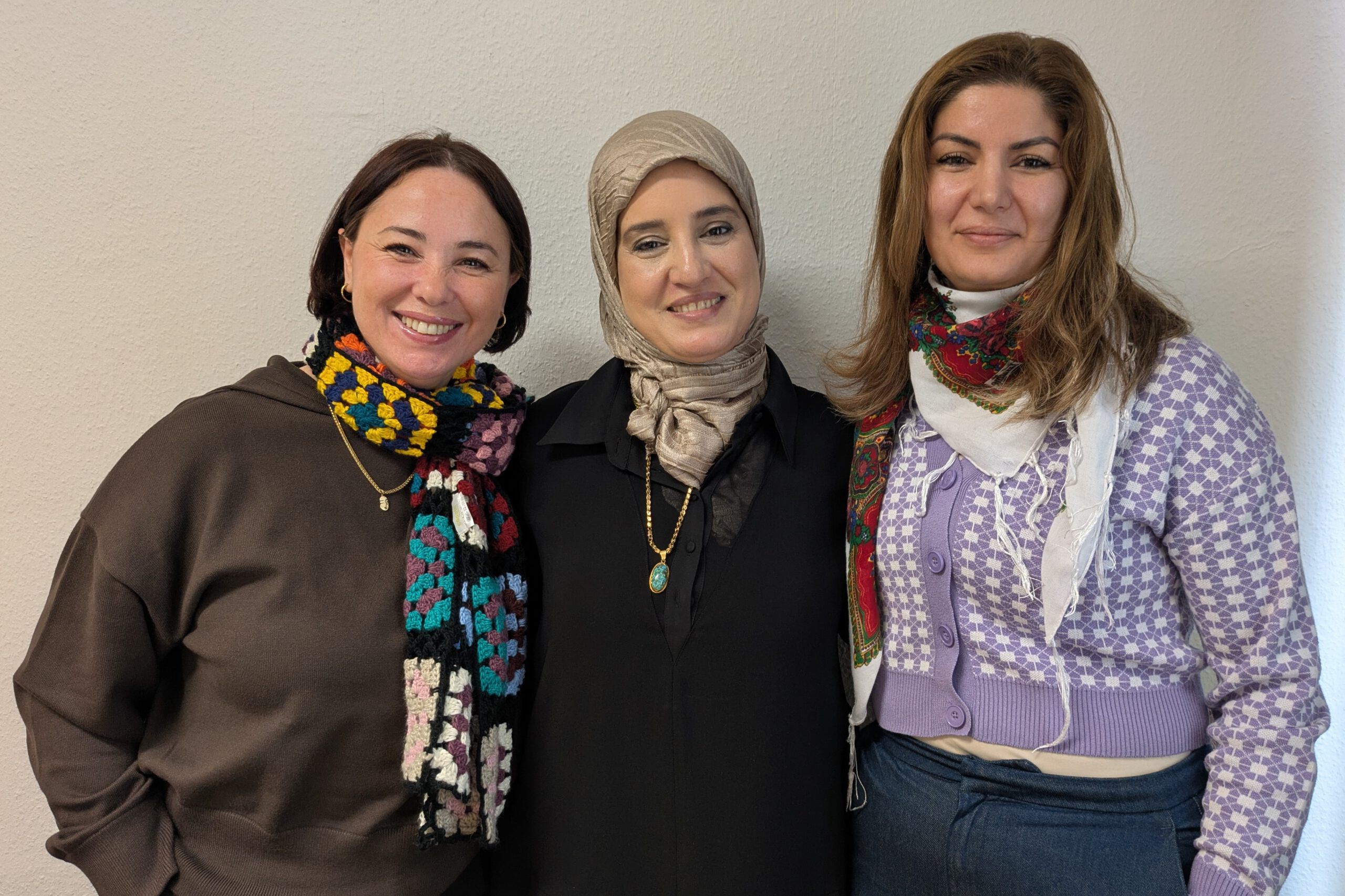 Fünf Frauen lächeln freundlich in die Kamera. Sie tragen farbenfrohe Kleidung uns stehen vor einem weißen Vorhang. Es sind die Deutschlehrerinnen aus den Integrationskursen.