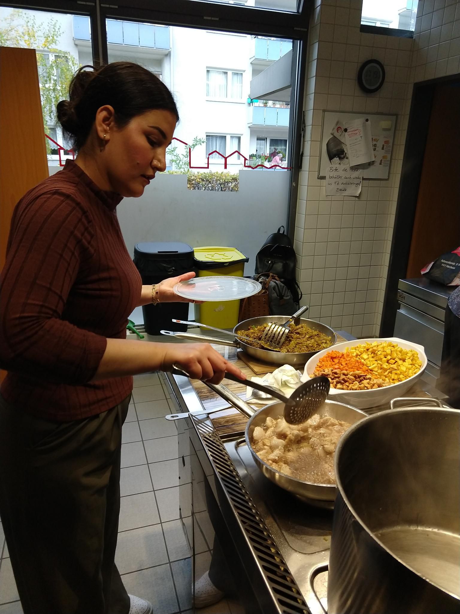 Vier Frauen sitzen an einem Tisch, eine weitere Frau steht daneben. Die Frauen lächeln in die Kamera. Im Hintergrund sind weitere Personen zu sehen.