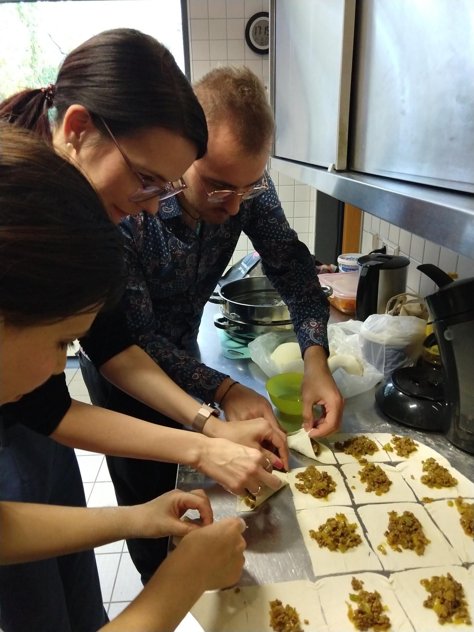Drei Frauen sitzen an einem Tisch, der Tisch ist für das Essen gedeckt. Im Hintergrund sind weitere Frauen, die sich unterhalten.