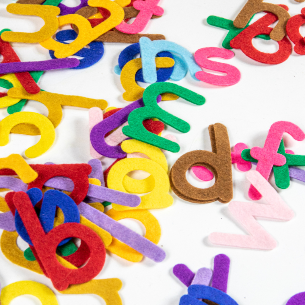 Bunte Filzbuchstaben liegen durcheinander auf einem weißen Tisch. Der Link führt zu Angeboten für Schulkinder. 