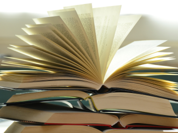 Ein Stapel aufgeschlagene Bücher. Das oberste Buch liegt wie ein Fächer auf den anderen.