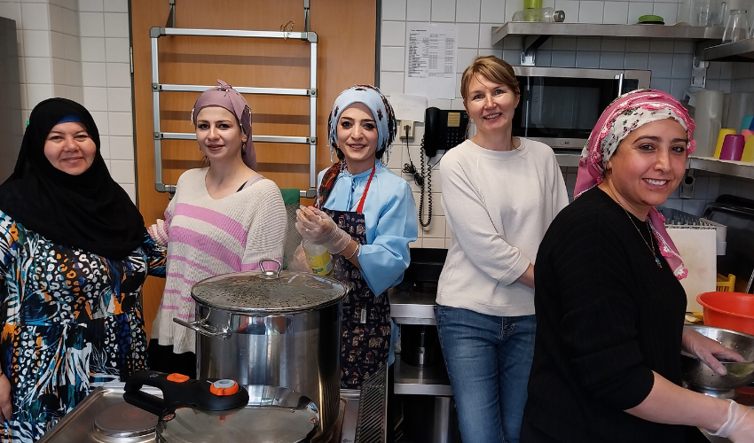 Teilnehmerinnen des Kochabends beim Arbeiten in der Küche. Sie blicken in die Kamera und lächeln.