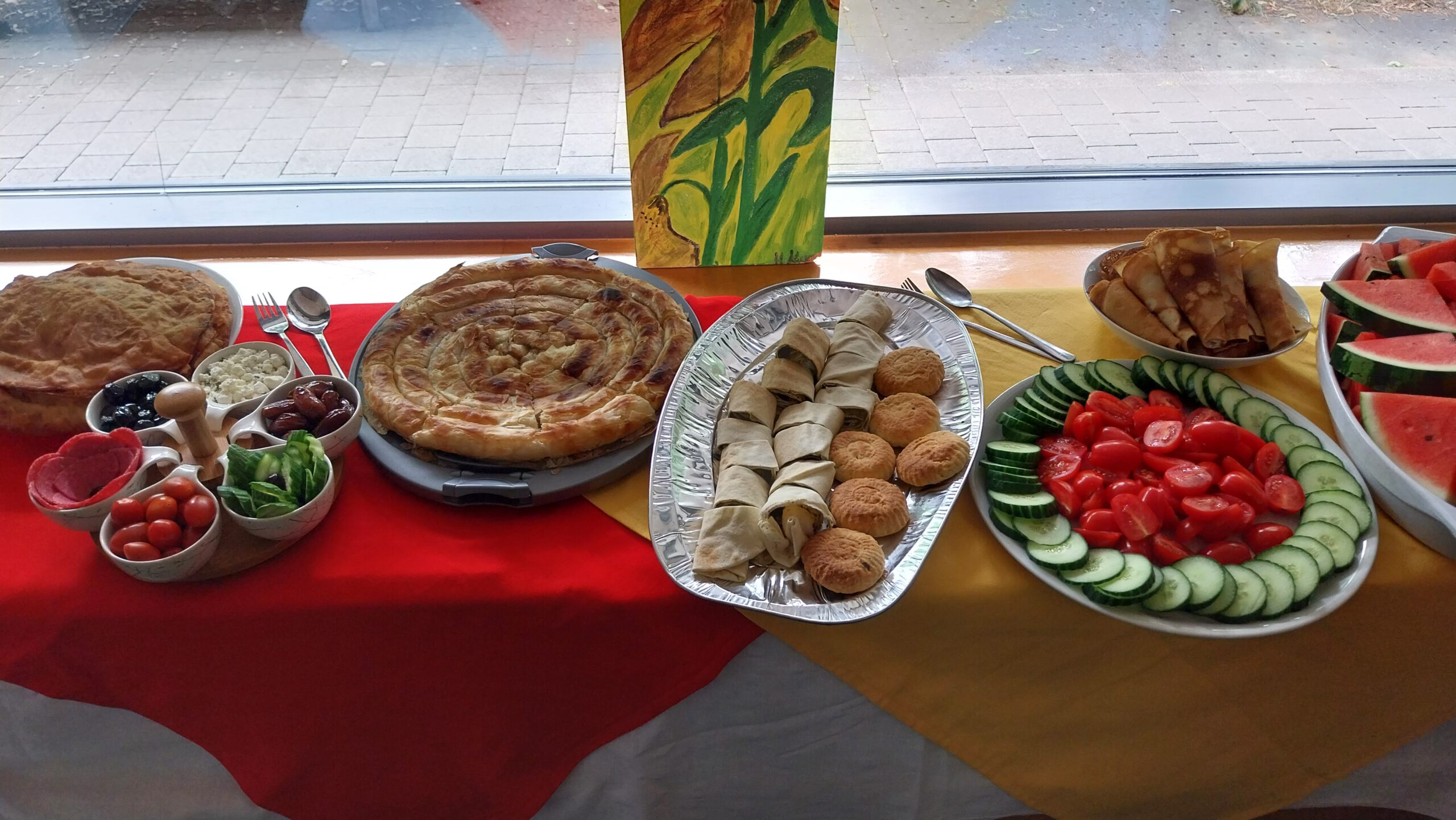 Auf einem Buffet stehen große Teller mit unterschiedlichen Speisen auf einer roten und gelben Tischdecke.