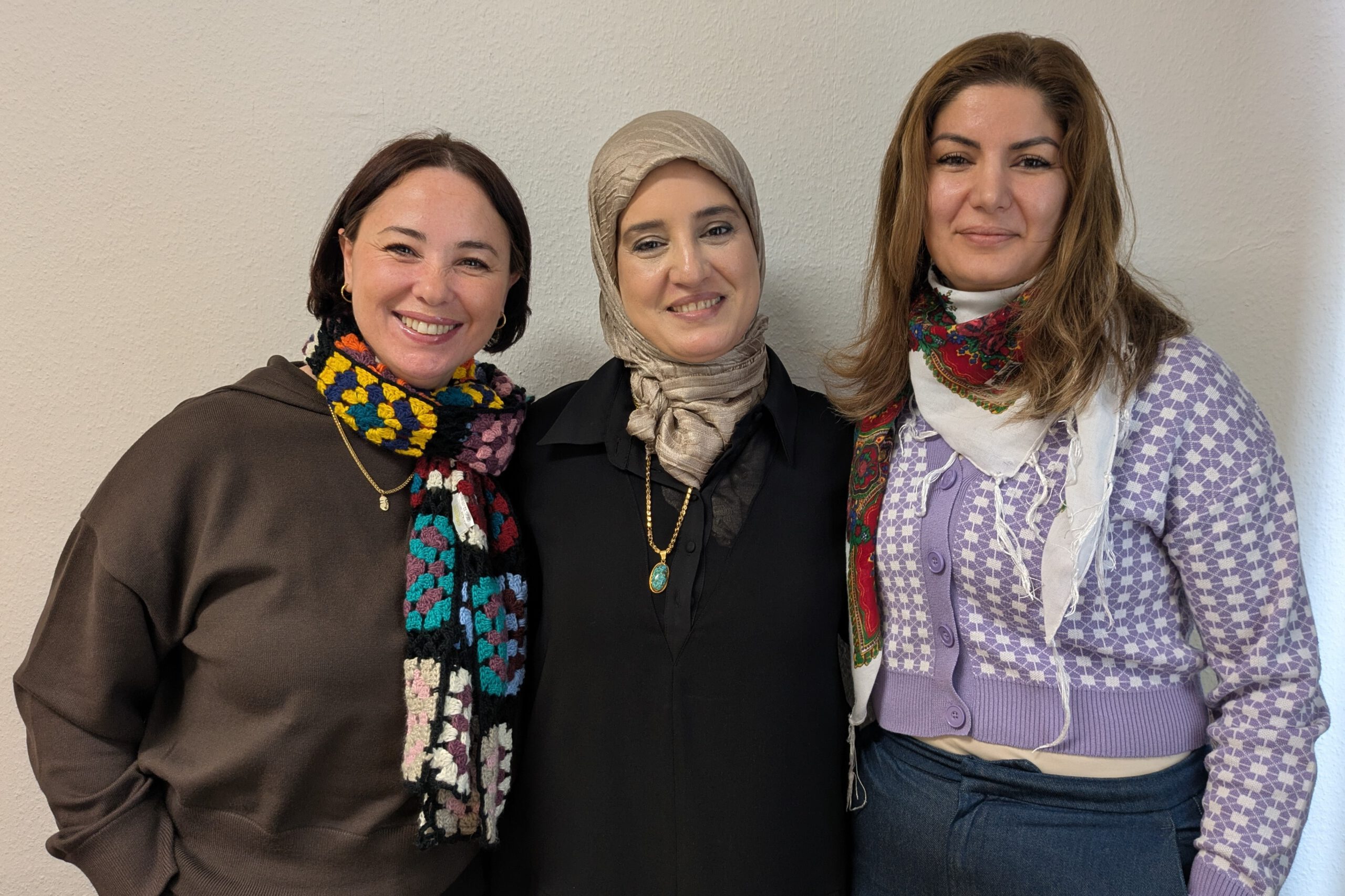 Fünf Frauen lächeln freundlich in die Kamera. Sie tragen farbenfrohe Kleidung uns stehen vor einem weißen Vorhang. Es sind die Deutschlehrerinnen aus den Integrationskursen.