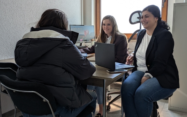Frau Hölscher und Frau Kurt sitzen mit einer Person am Tisch im Beratungsbüro. 