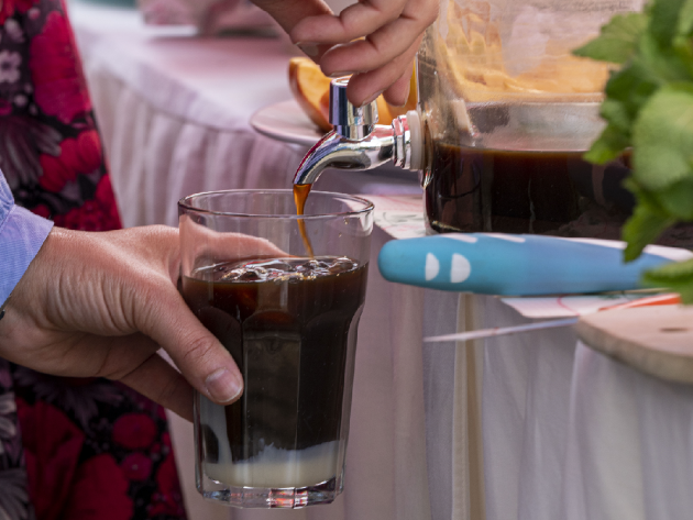 Eine Person lässt ein dunkles Getränk aus einem Glasspender in ein Glas ein.