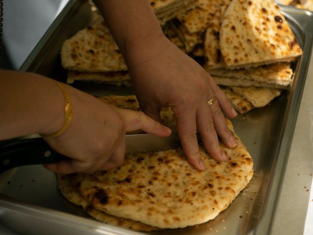 Zwei Hände schneiden ein flaches, rundes Brot mit hellem Teig.