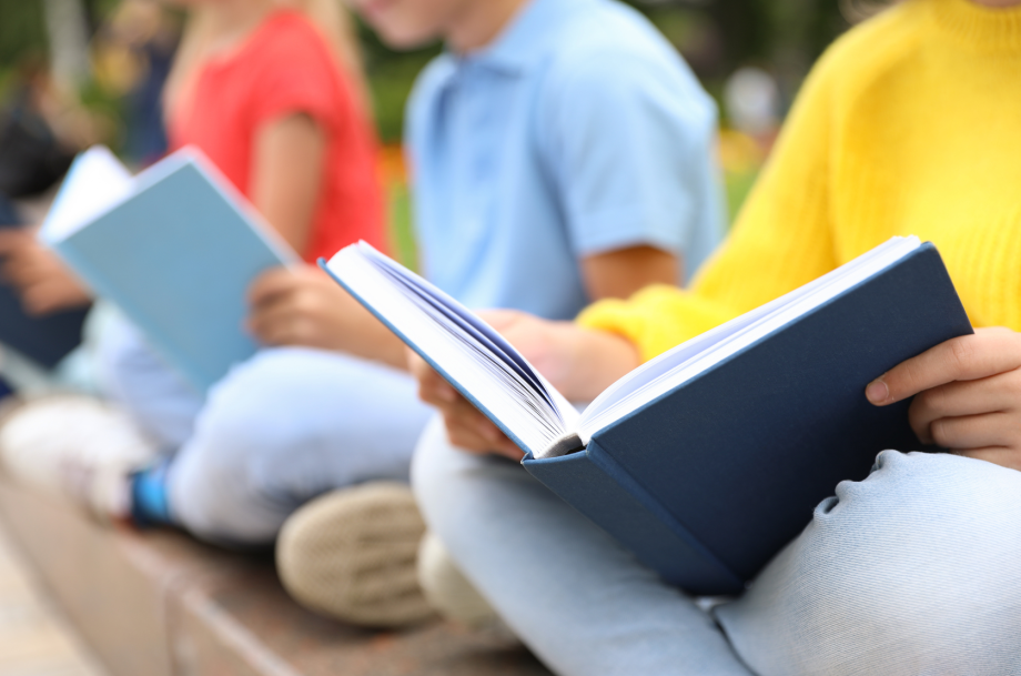 Kinder in bunten Kleidern sitzen auf einer Mauer und lesen.