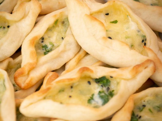 Man sieht ovale Teigtaschen, die mit Käse, Kräutern und Schwarzkümmel gefüllt sind.